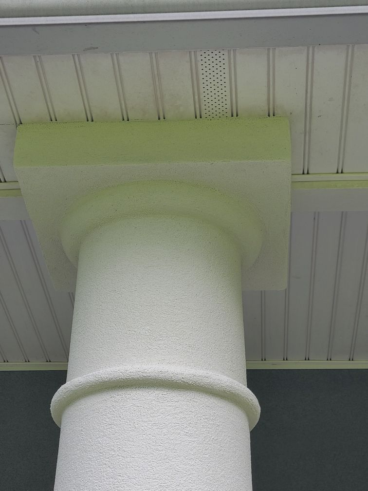 White decorative column under a light green ceiling beam outdoors