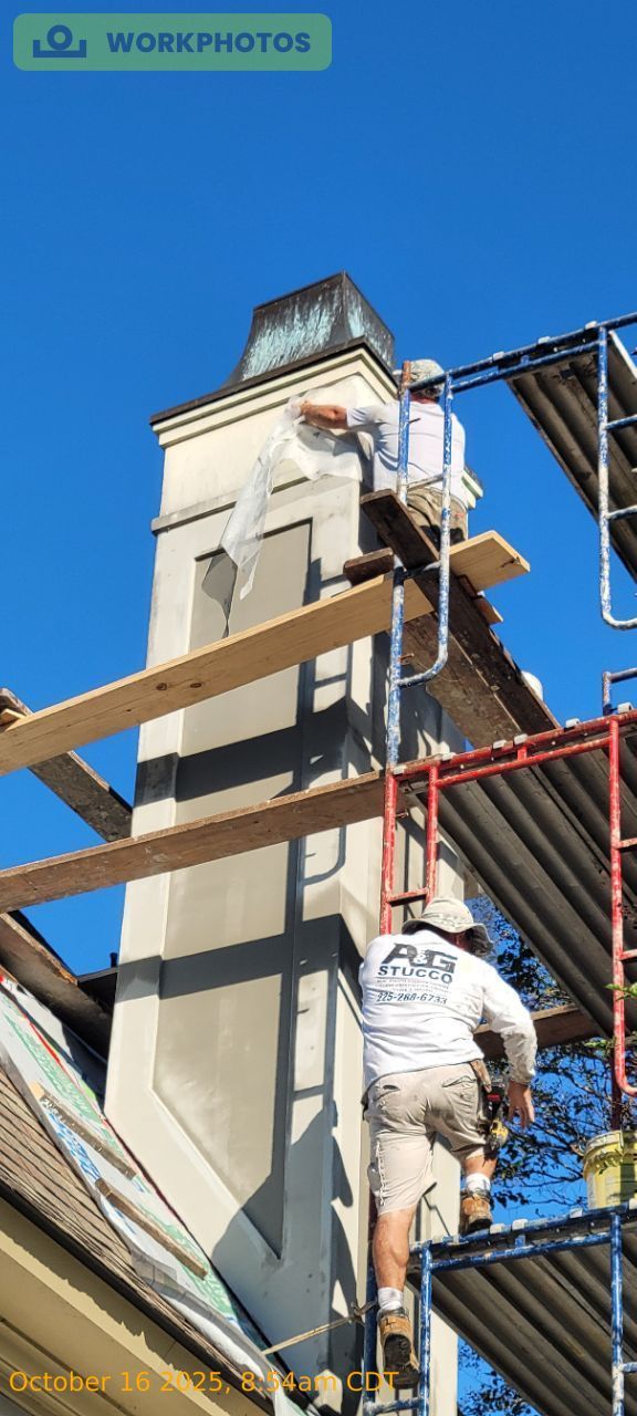 Worker on scaffolding painting a tall white building against a blue sky.
