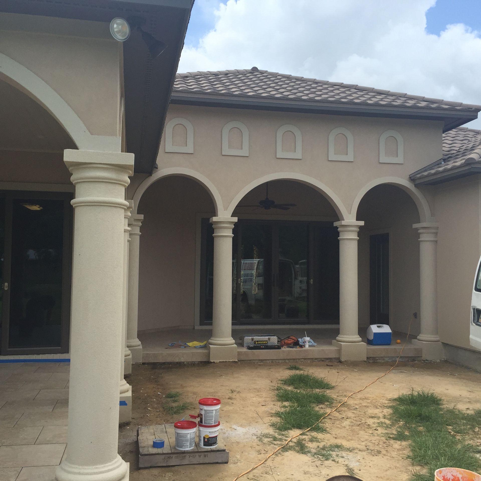 Front view of a beige house with arched columns and a dirt front yard under construction.