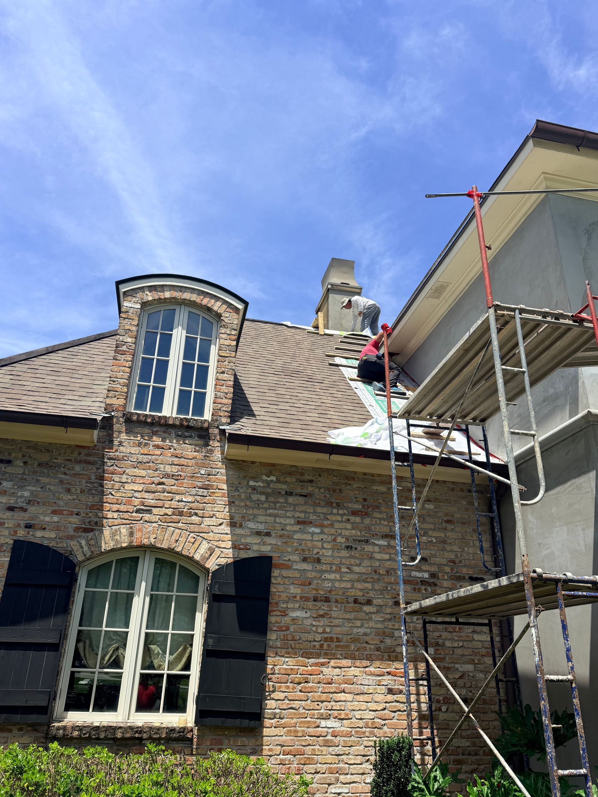 Brick house roof under repair with scaffolding beside a blue sky