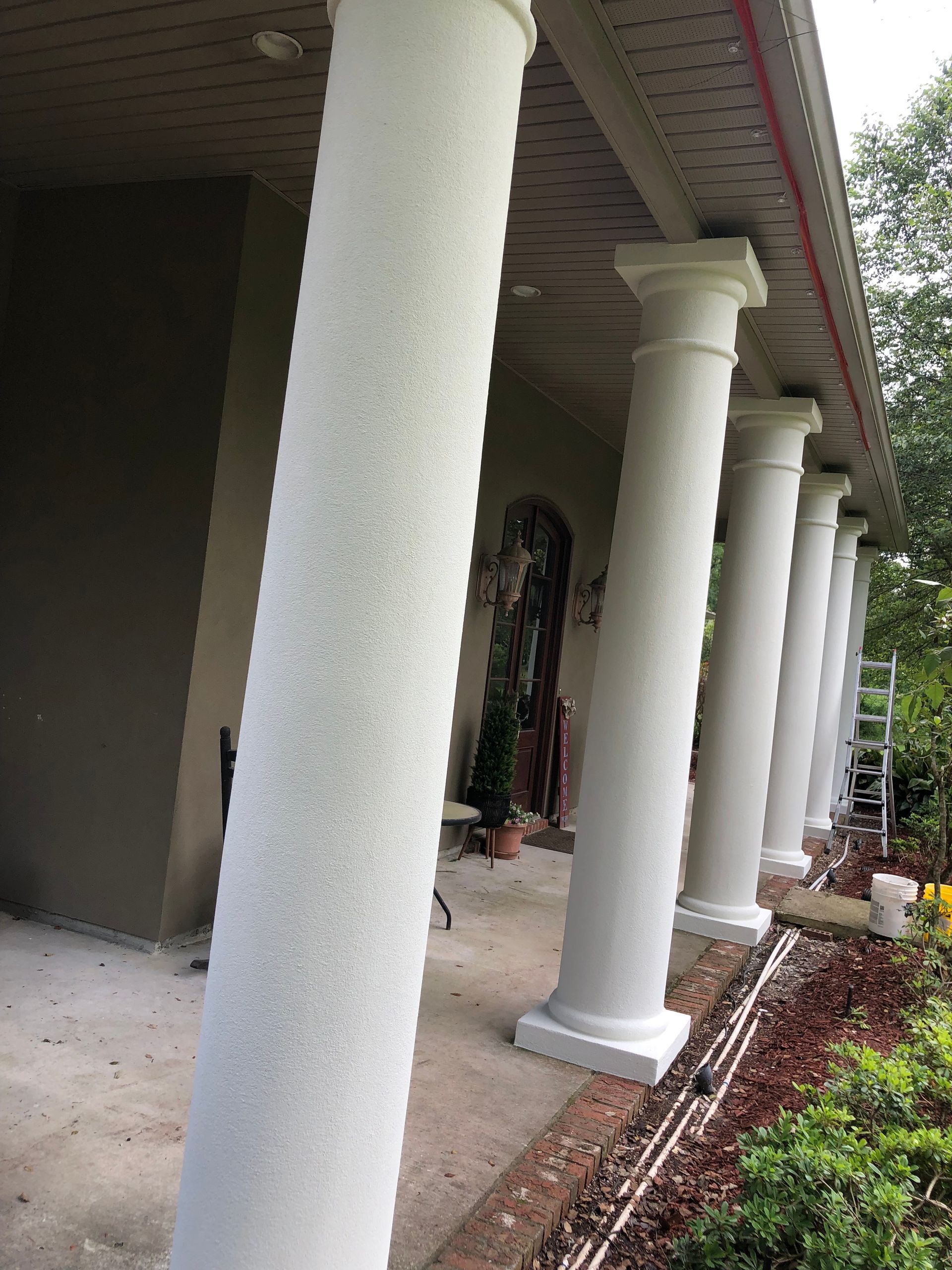 Covered front porch with white columns and potted plants along the walkway.