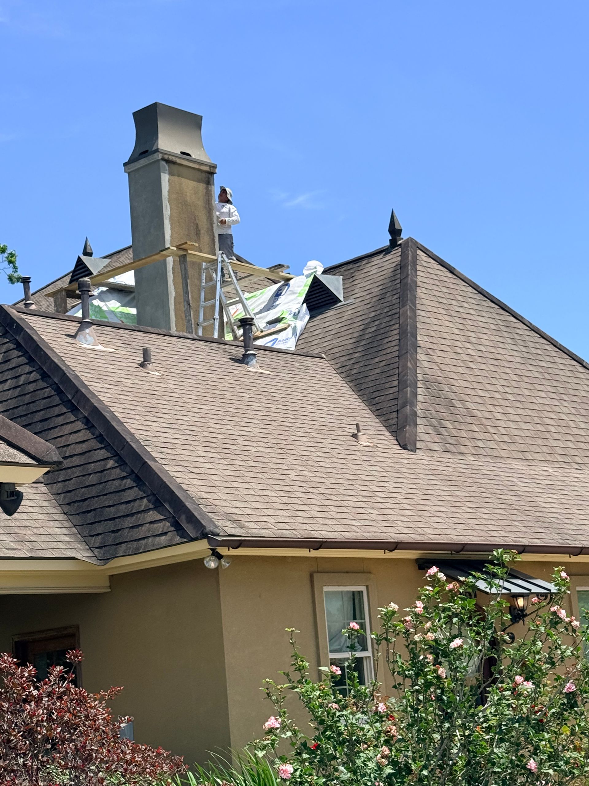Suburban house roof with storm damage near the chimney, missing shingles and debris under a blue sky
