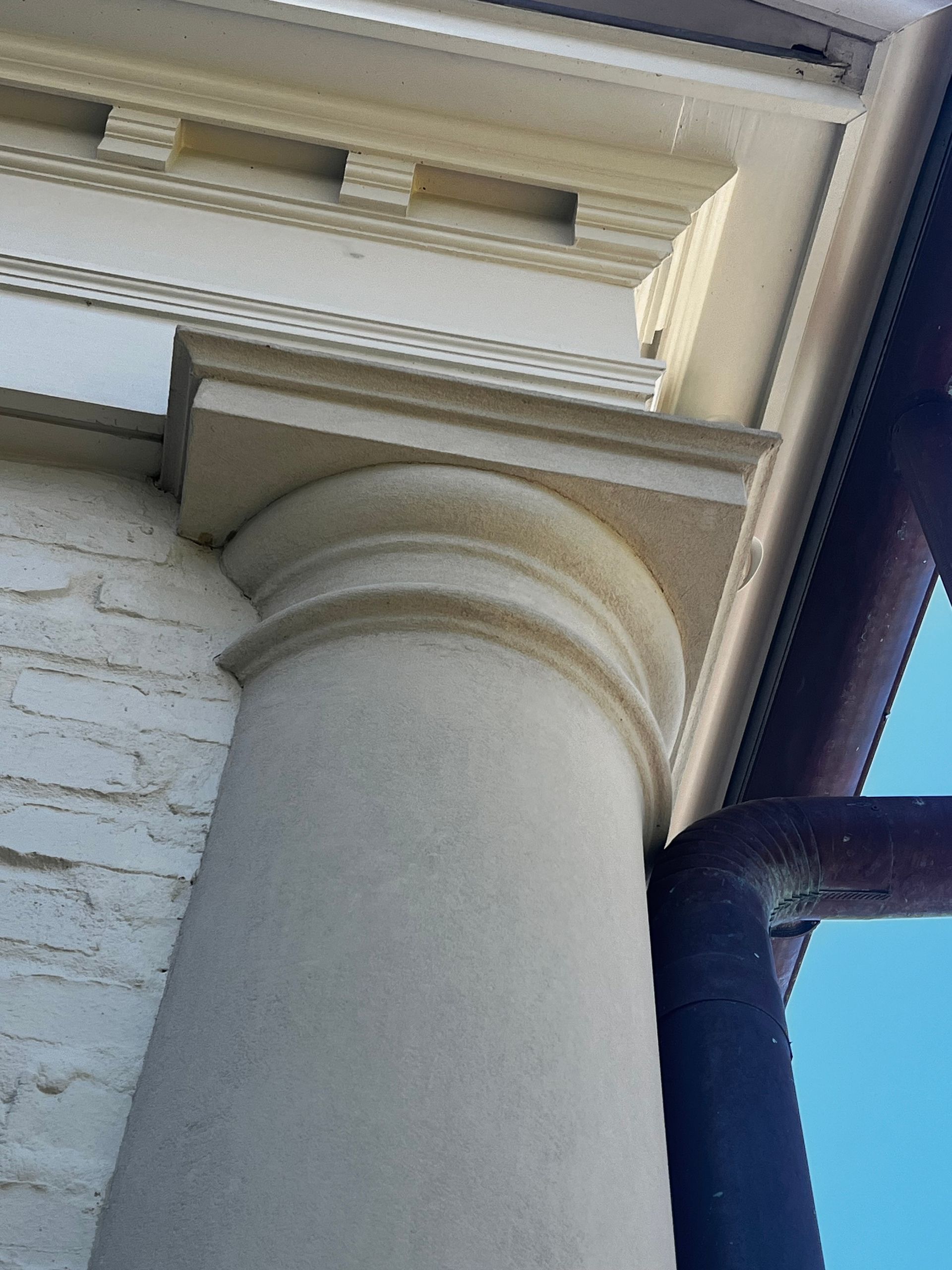 Close-up of a white classical porch column under a roof eave against a blue sky
