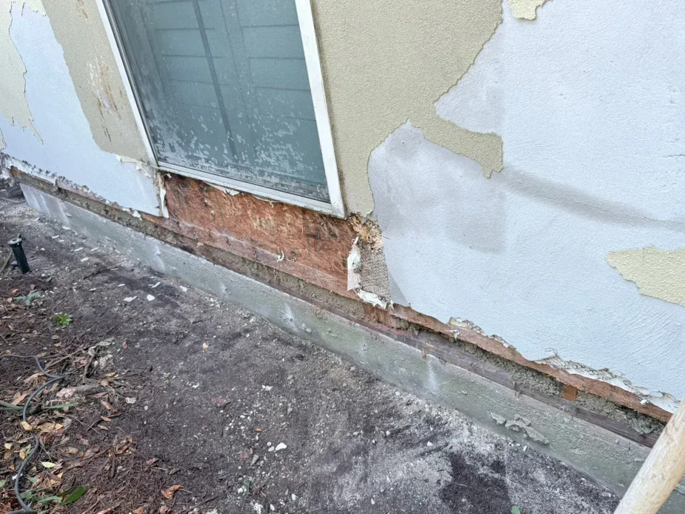 Damaged exterior wall with peeling paint and cracked stucco near a door and dirt ground