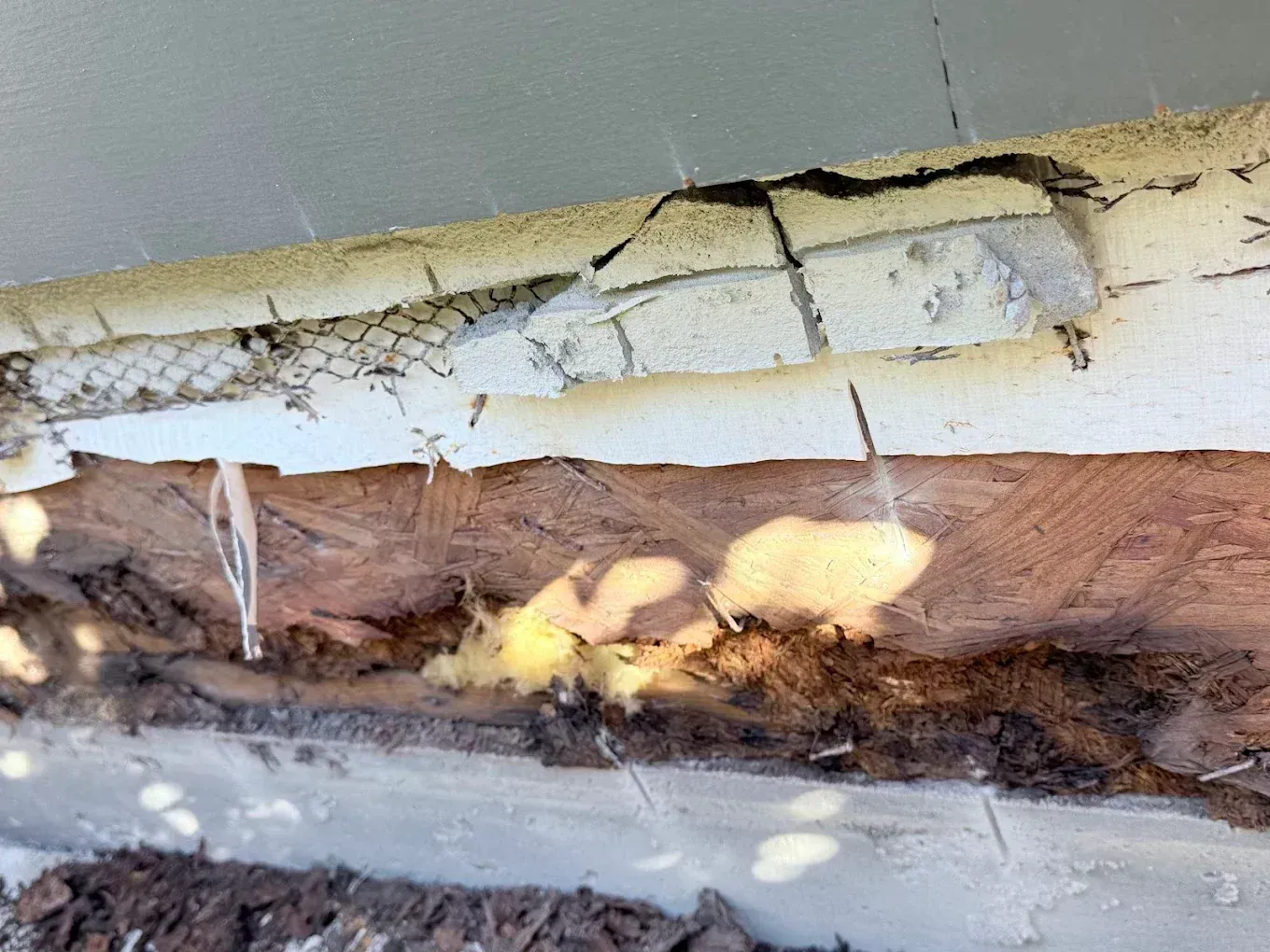 Peeling white pipe insulation exposing brown fiberglass and damaged material underneath