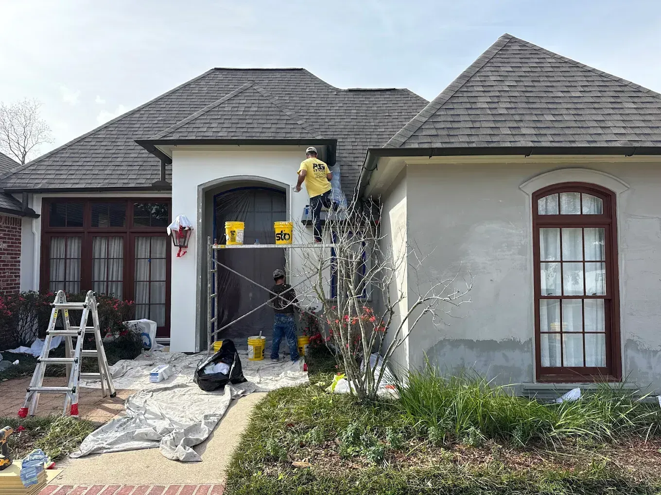 Front of a house under renovation with ladders, tools, and protective coverings at the entrance