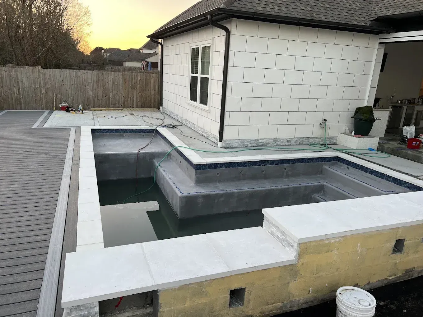Backyard in-ground pool under construction beside a white house at dusk