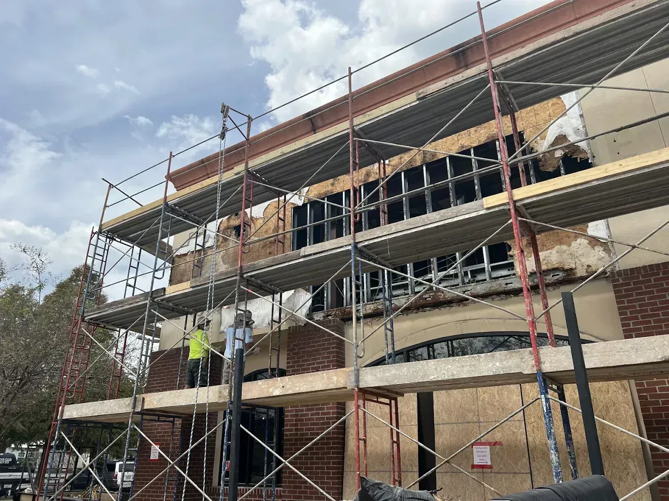 Construction site with scaffolded building facade, workers, and unfinished windows under a cloudy sky