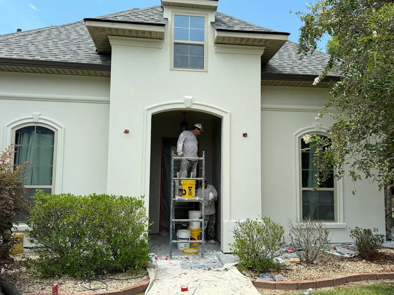 Worker on ladder outside house entrance, painting or repairing the doorway.