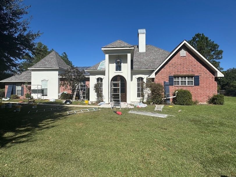 Suburban brick-and-stone house with a manicured lawn under a clear blue sky