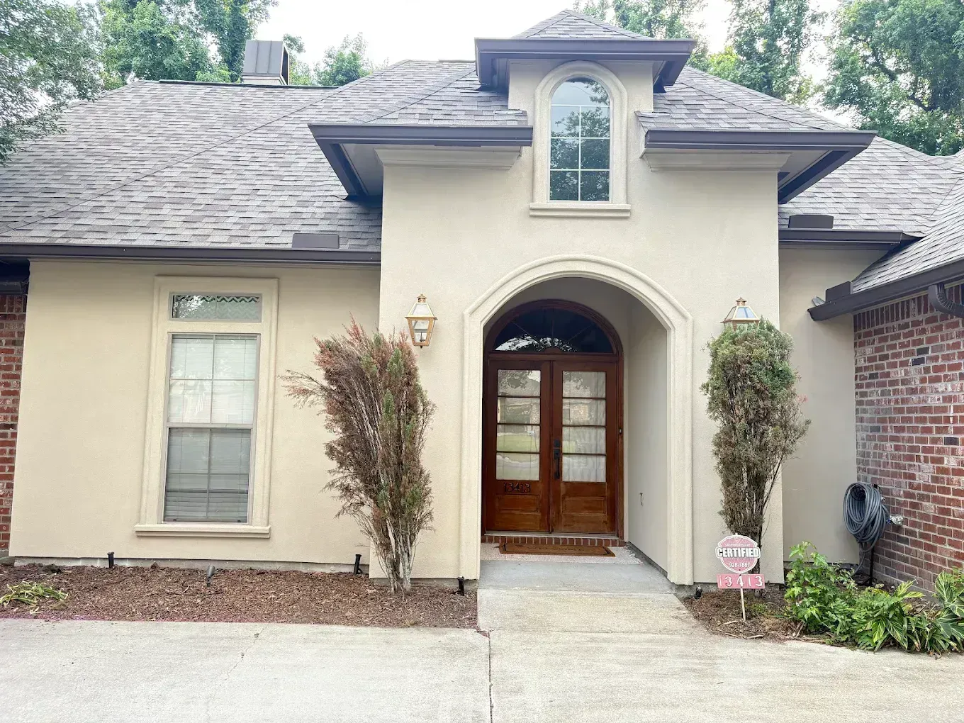 Front view of a beige house with arched wooden front door and a short walkway.