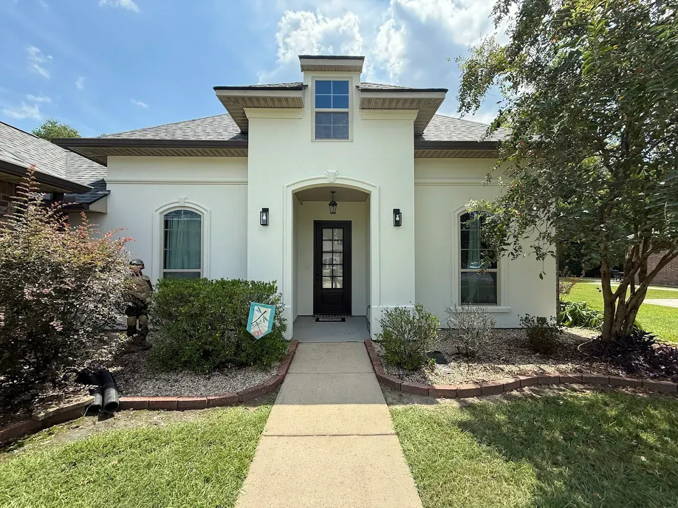 Front view of a cream stucco house with a centered arched entry and landscaped front yard.