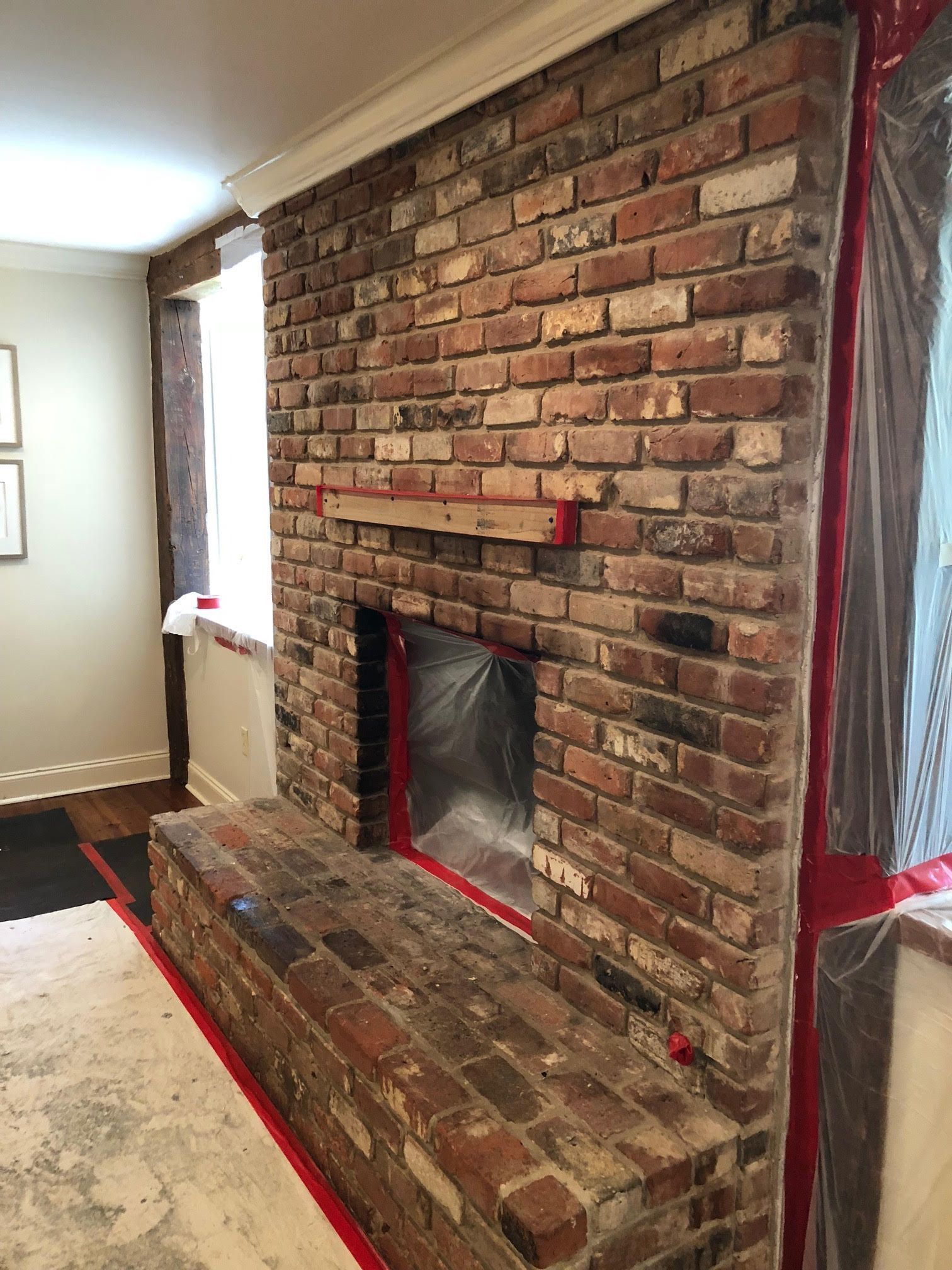 Brick fireplace under renovation, with exposed bricks and plastic covering the opening in a living room