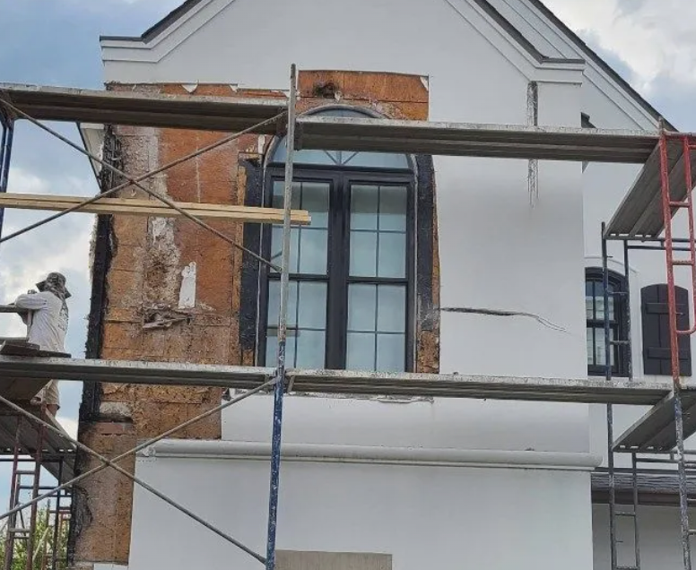 White house facade under scaffolding, with exposed brick around a tall central window and visible exterior cracks