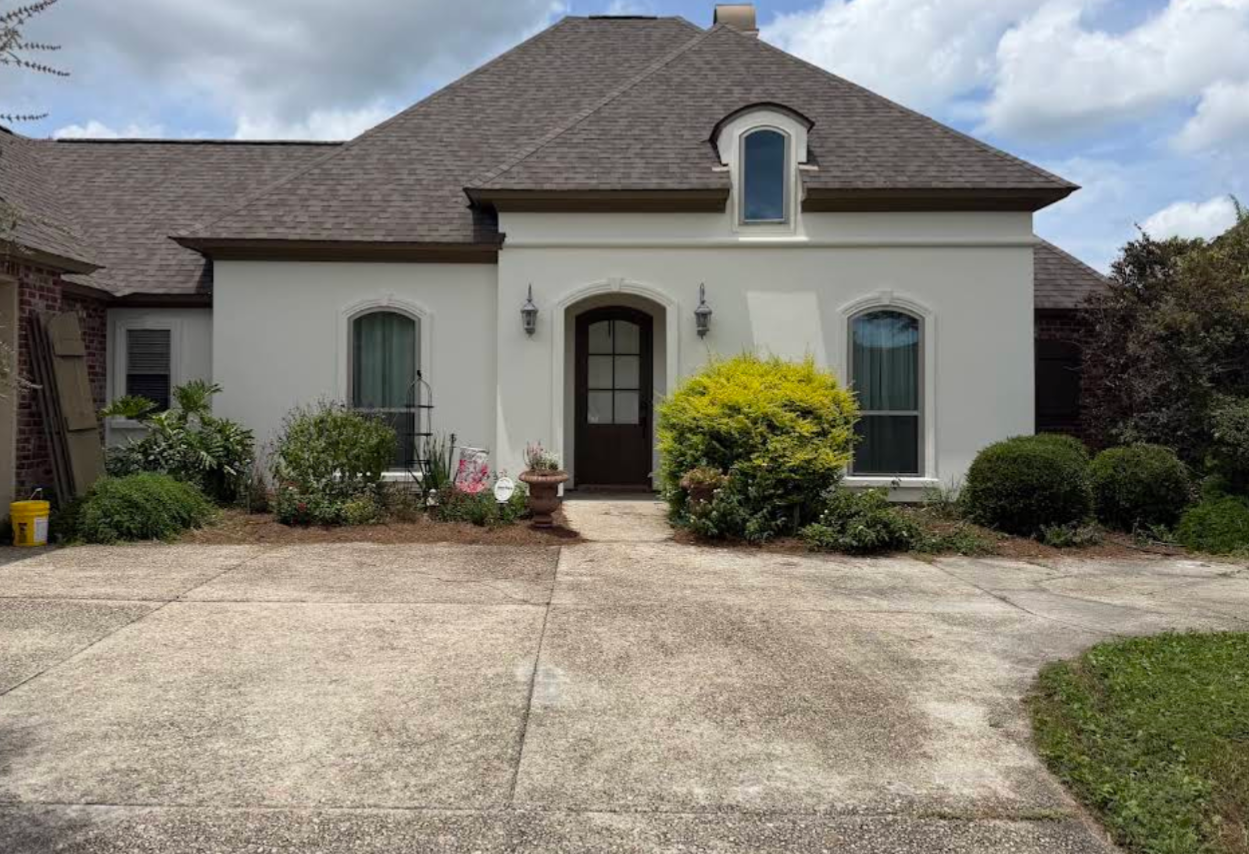 Suburban house with stucco exterior, arched front door, driveway, and landscaped shrubs under cloudy sky