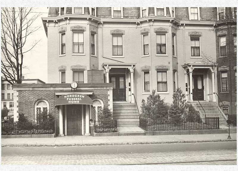 Black and white photo of a three-story building with multiple windows and a covered entrance.