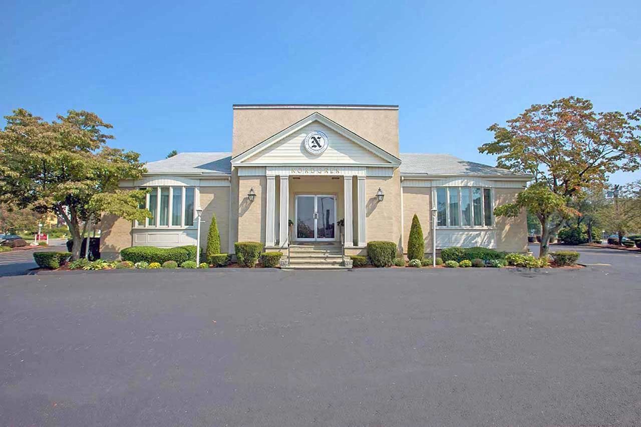 Exterior view of a beige building with a central entrance, flanked by windows and trees on a clear, sunny day.