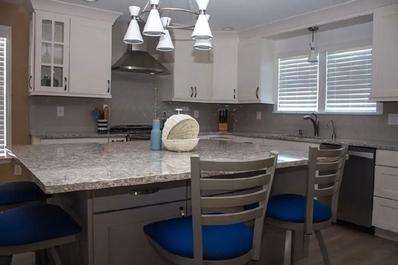 A kitchen with white cabinets , granite counter tops , and blue chairs.