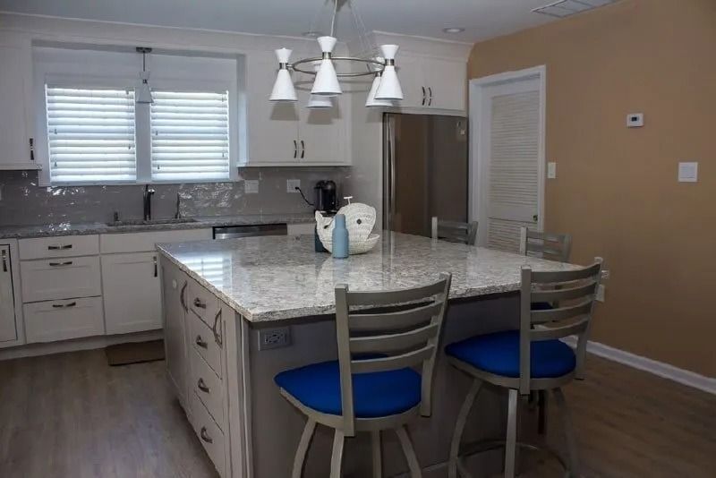 A kitchen with white cabinets and a large island with blue chairs.