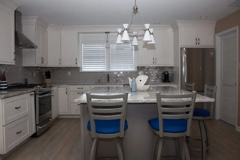A kitchen with white cabinets , stainless steel appliances , a large island , and blue chairs.