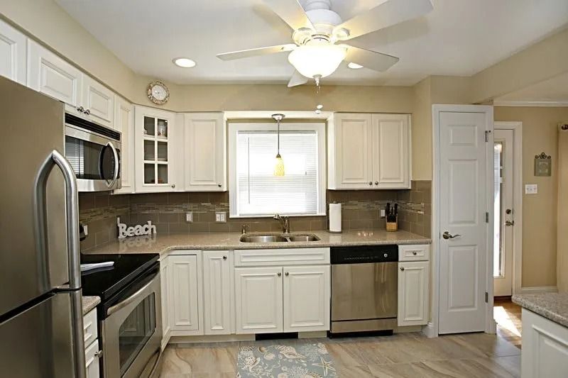 A kitchen with white cabinets , stainless steel appliances and a ceiling fan.