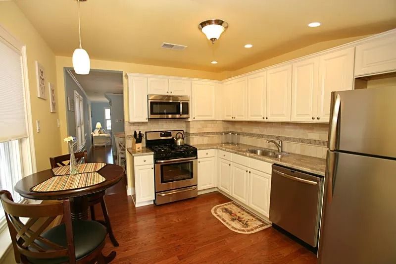 A kitchen with white cabinets , stainless steel appliances , a table and chairs.