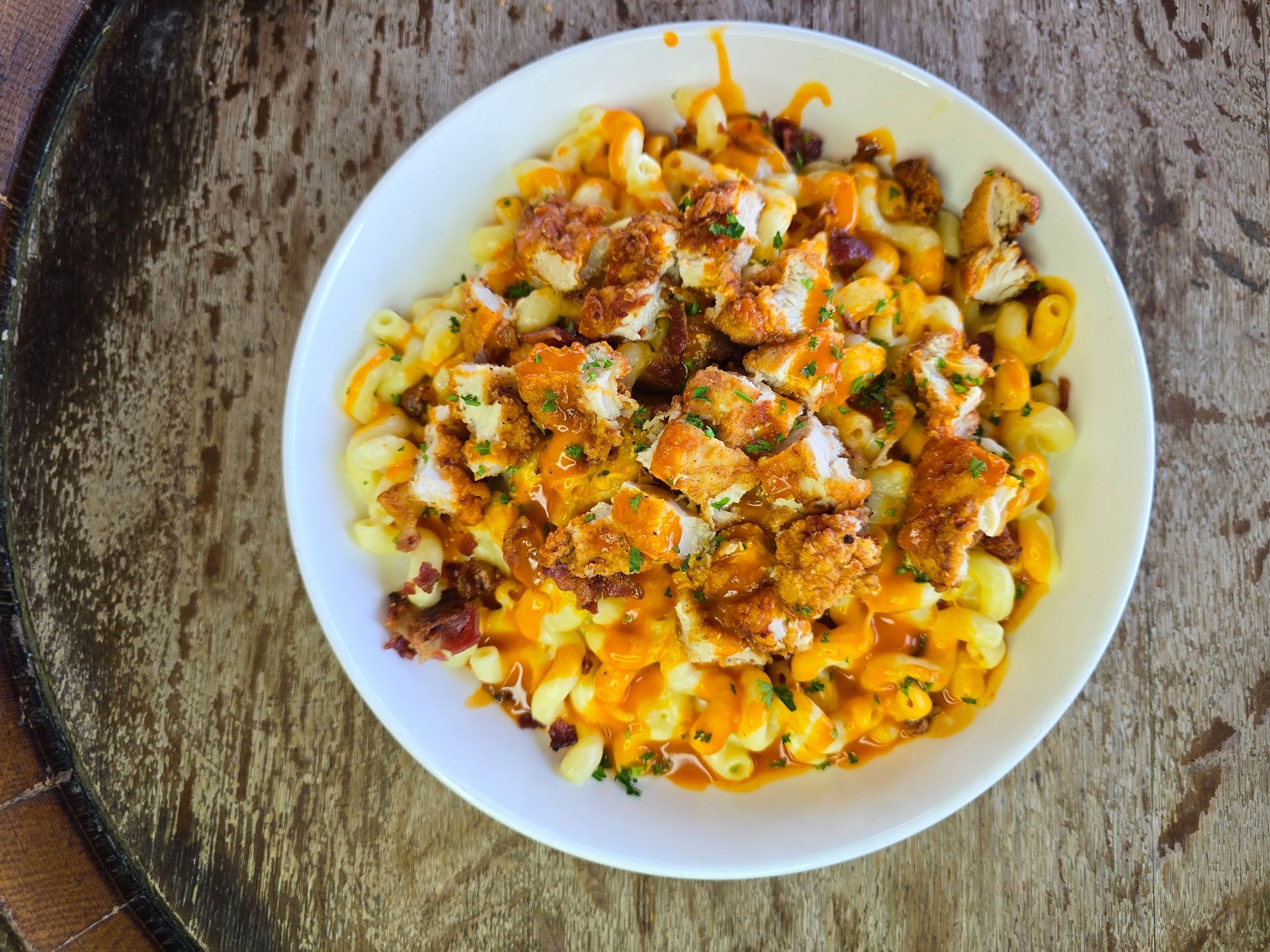 Mac and cheese with diced chicken in a white bowl on a wooden surface.