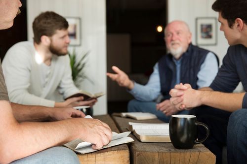 A group of men are sitting around a table talking to each other.