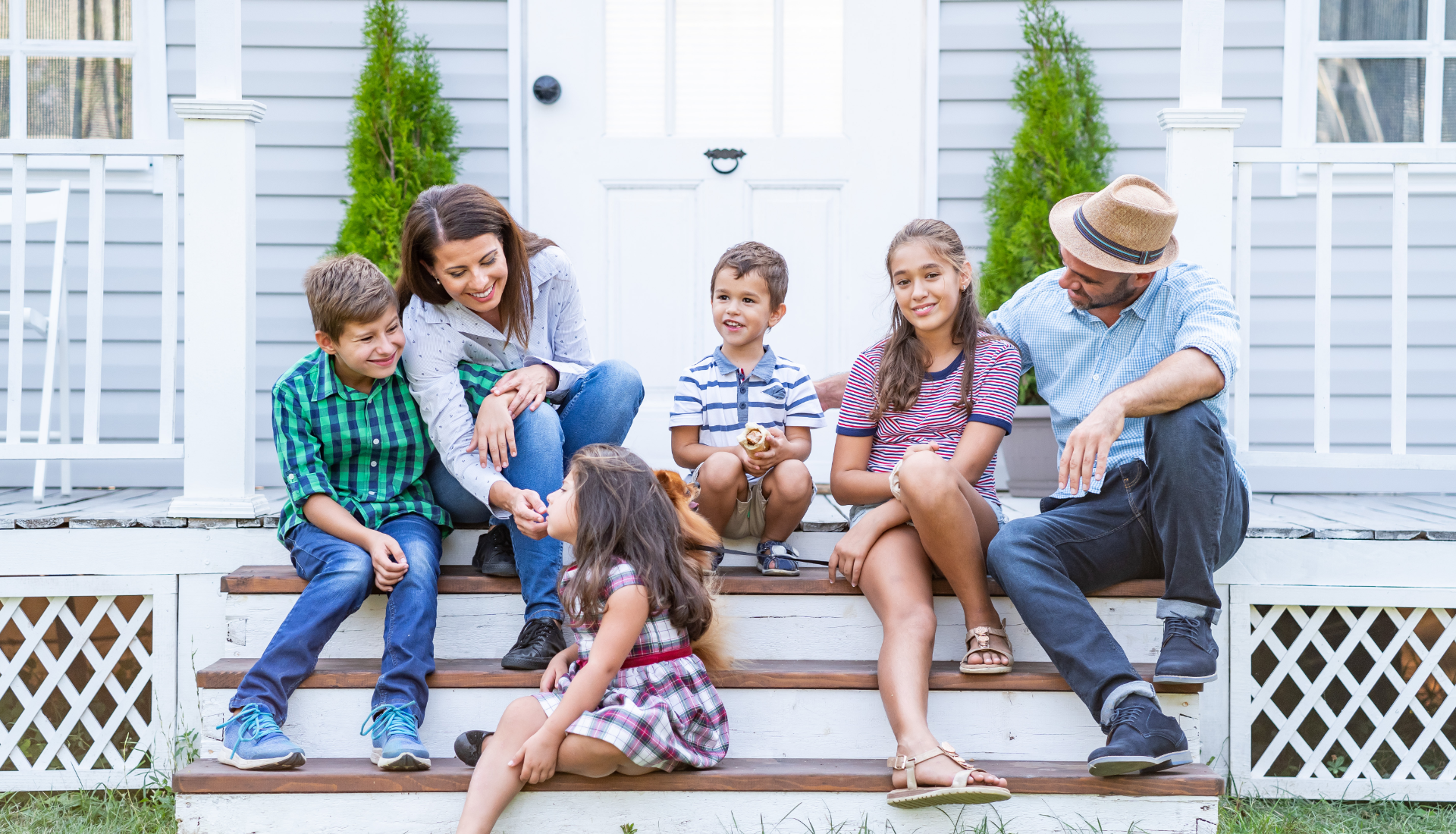 Family outdoors, smiling and talking; man gesturing, elderly man sitting, young girl, and blonde women.
