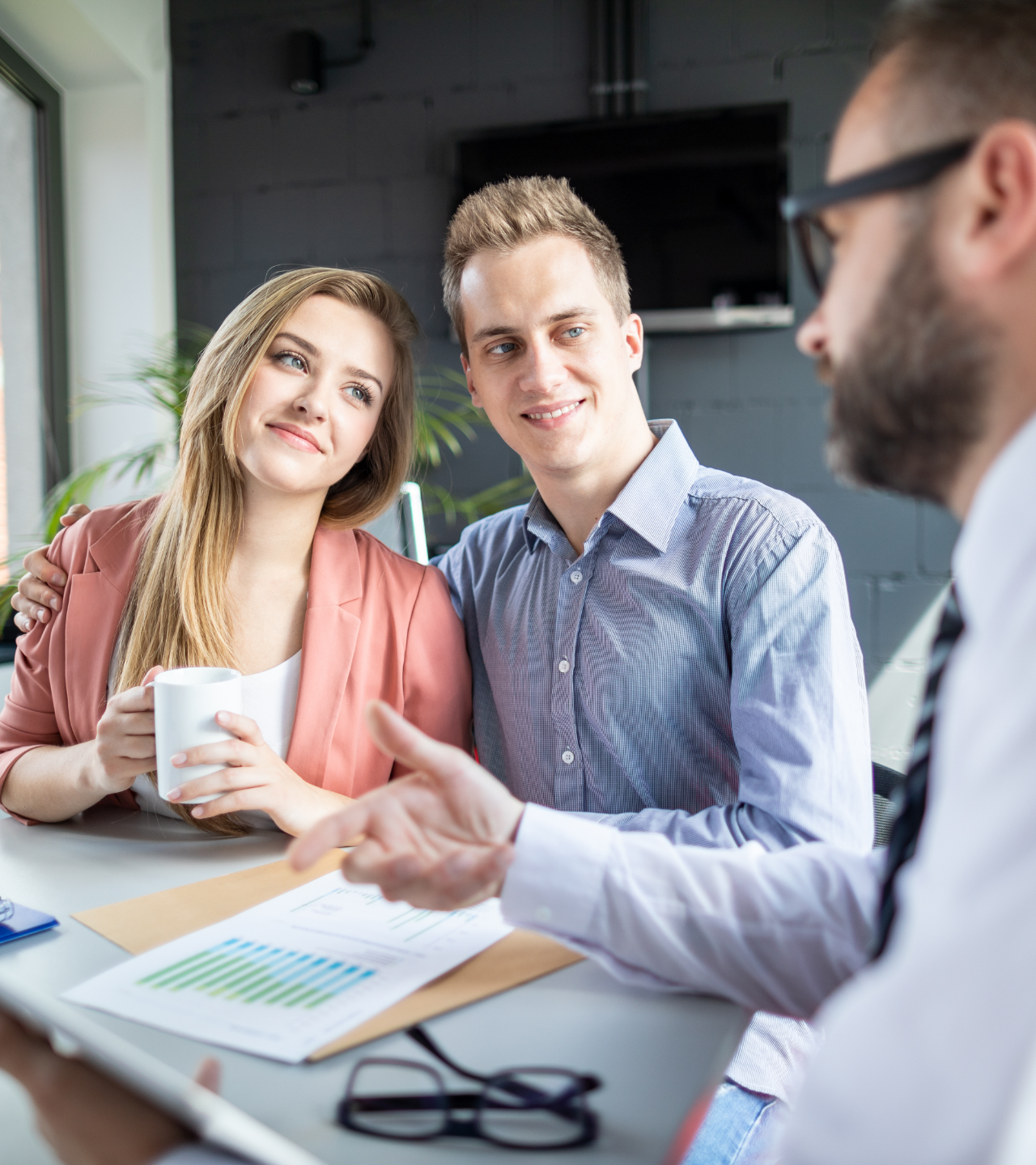 Couple looking at document with person at desk, smiling.