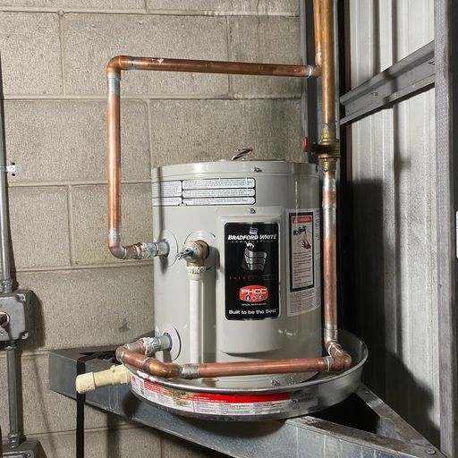 Old water heater with copper pipes in a utility room beside a window