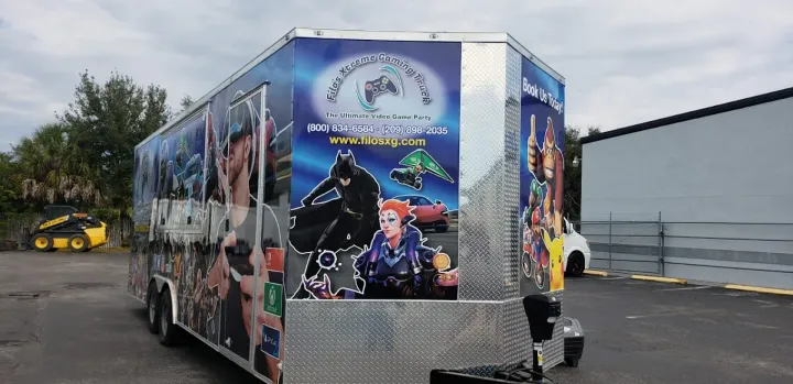 Game trailer with comic book art on the sides and a Batman image in the center. Trailer is parked on a dark gray lot.