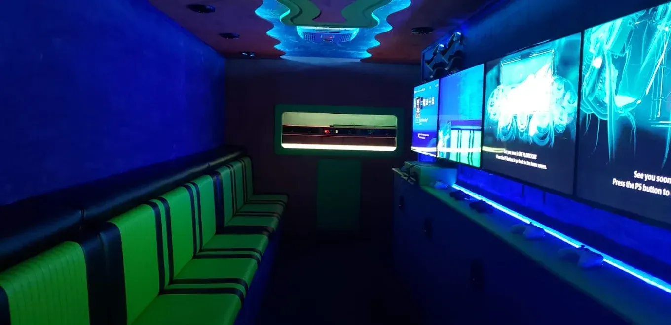Interior of a game truck with green seating, blue walls, and screens displaying graphics.