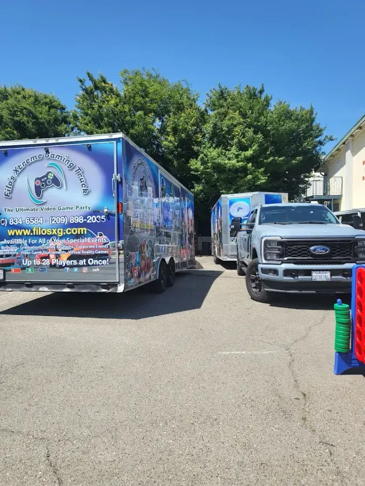 Two gaming trailers and a truck parked outdoors on a sunny day.
