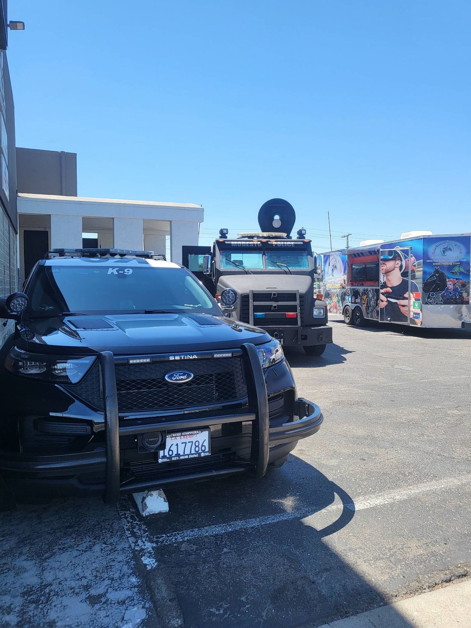 Black police SUV parked next to a large armored vehicle and a colorful bus on a sunny day.