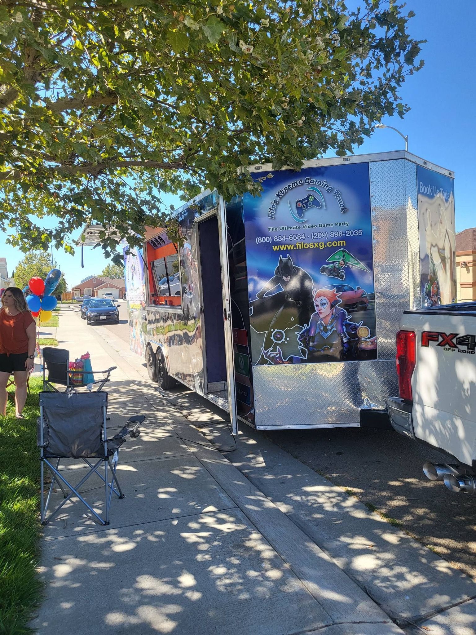 Food truck on a sunny street, featuring a large graphic, parked next to a sidewalk with a chair set up.