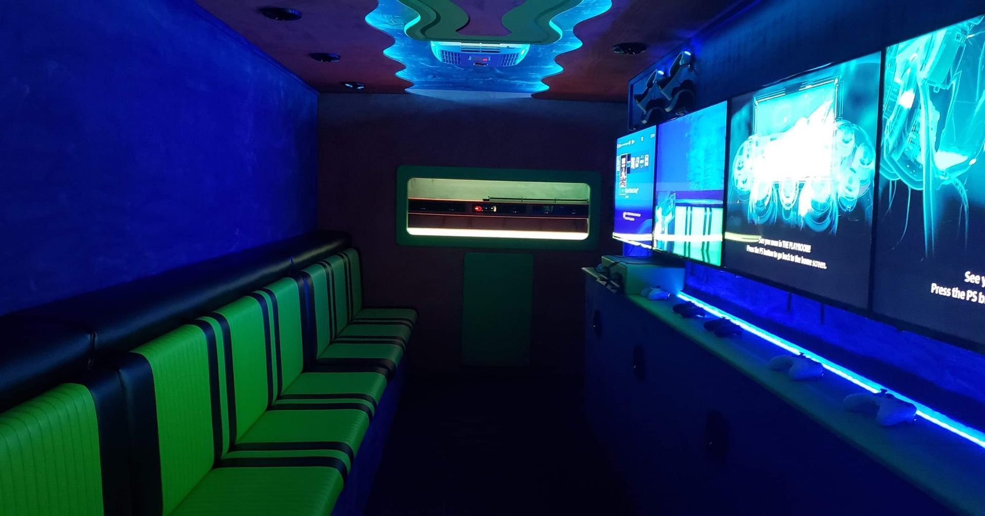 Interior of a gaming truck with neon green and blue lights, screens, and seating.