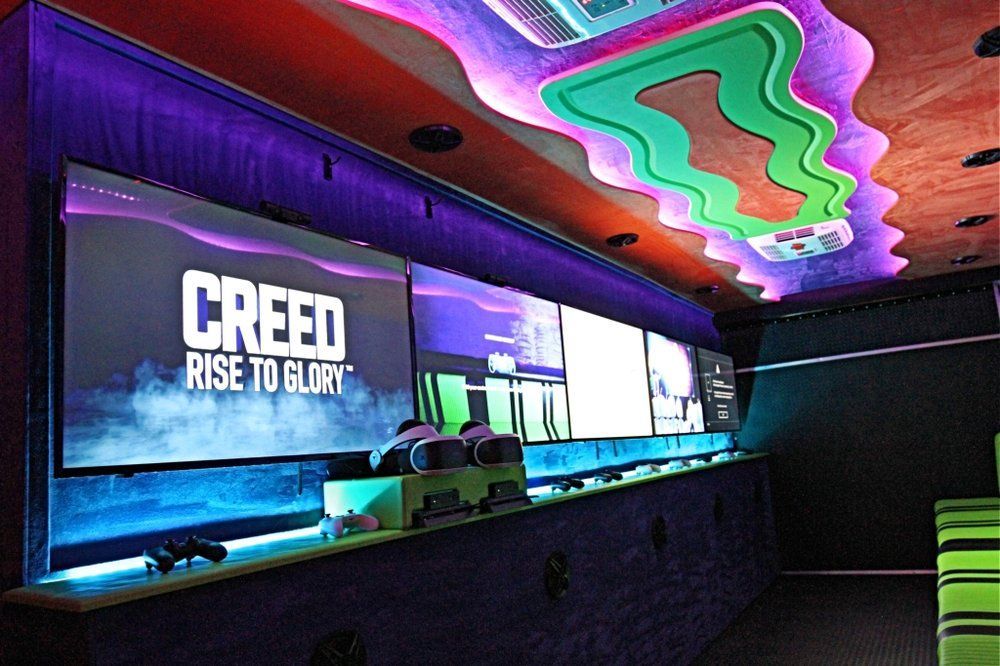 Inside a gaming bus, large screens display games. The ceiling glows with colorful lights.