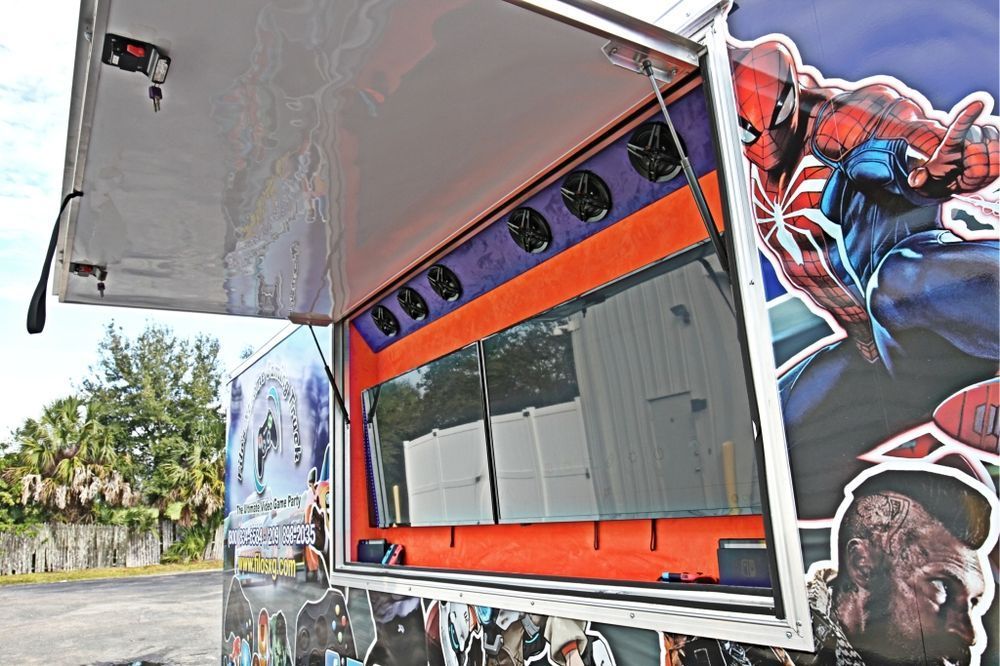 Side view of a Spider-Man themed mobile gaming truck with an open window displaying multiple screens.