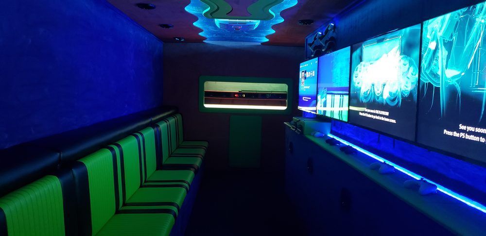 Interior of a gaming truck with rows of neon green seats, large screens, and blue lighting.