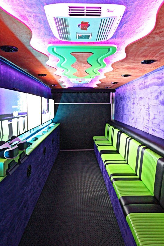 Interior of a colorful gaming bus, with rows of seating, screens, and neon lighting.