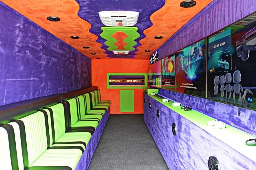 Inside a colorful game truck: Purple and orange walls, green seats, screens with games.