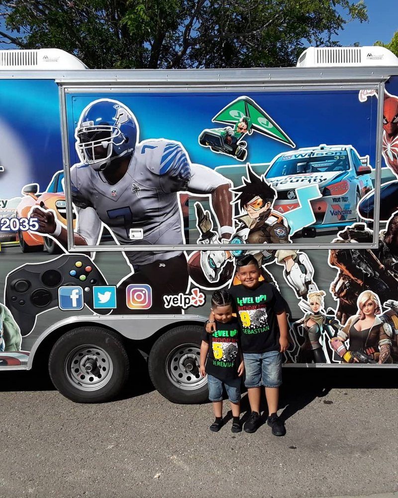 Two kids stand in front of a game truck with sports and video game graphics.