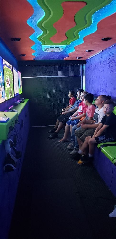 Inside a brightly colored gaming truck, a group of kids sit, facing screens, focused on a game.