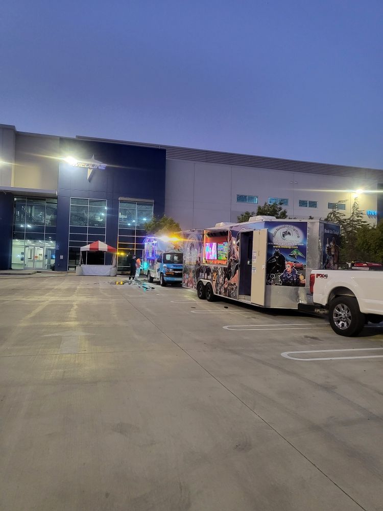 Food trucks parked outside a building. Several are illuminated with colorful lights. Dusk setting.