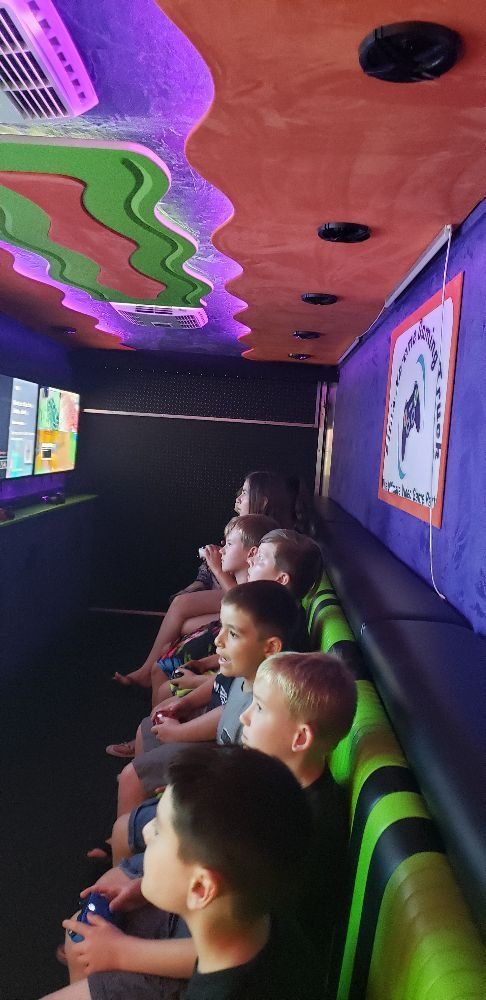 Children playing video games inside a colorful gaming van, with neon lighting and multiple screens.