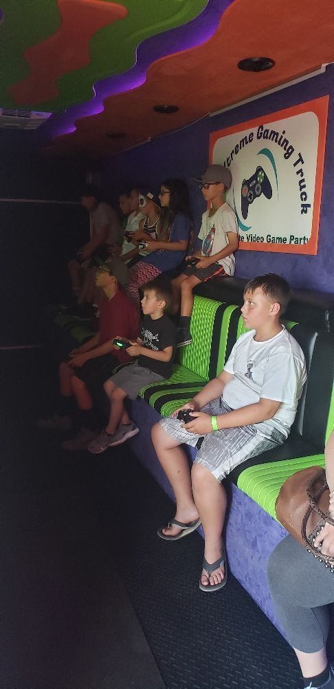 Inside a gaming truck, several people sit playing video games, controllers in hand.