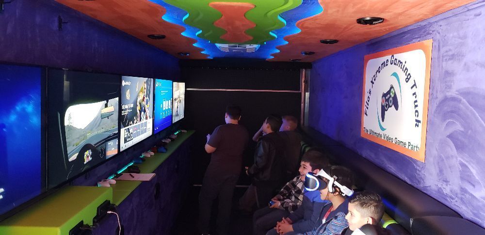 Inside a gaming truck, people play video games on multiple screens. The ceiling has a colorful design.