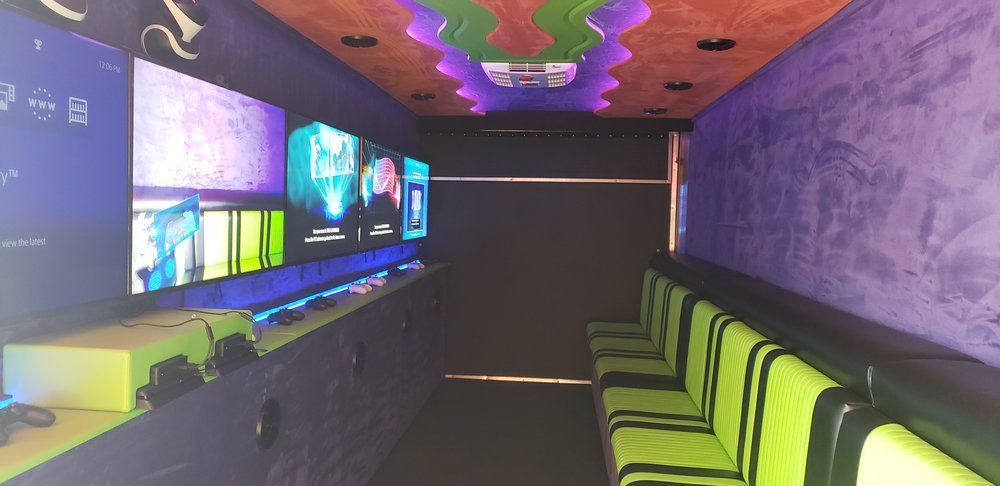 Inside a gaming truck, TVs line one wall, seats on the other. Ceiling lights with neon colors.
