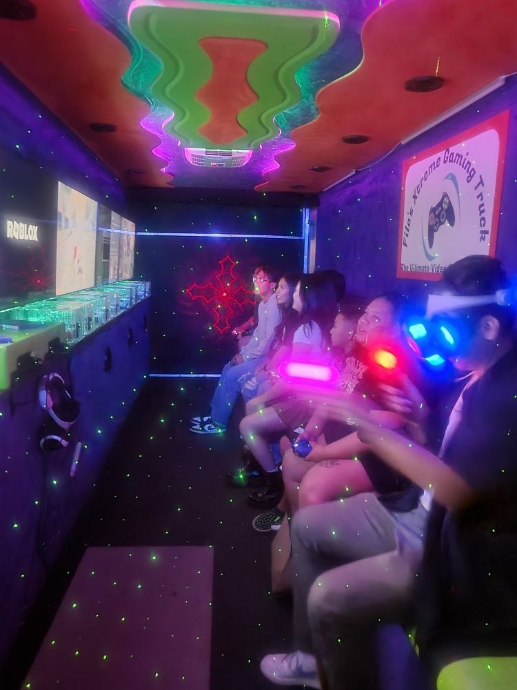 People playing video games inside a colorful gaming truck, using controllers and wearing VR headsets.